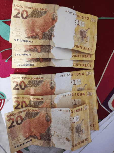 Notas de R$ 20 do Banco Central do Brasil empilhadas sobre uma superfície colorida.