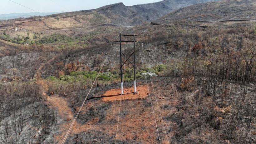 Torres de transmissão de energia elétrica em uma área afetada por queimadas, com vegetação queimada ao redor.
