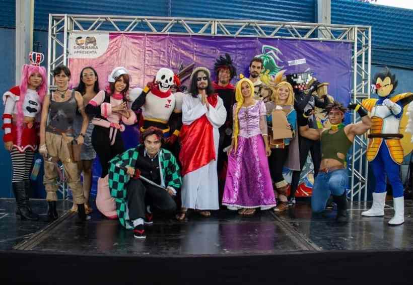 Um grupo de pessoas vestidas em trajes de cosplay, representando personagens de animes e jogos. Eles estão posando juntos em um palco, com um fundo colorido e decorativo.