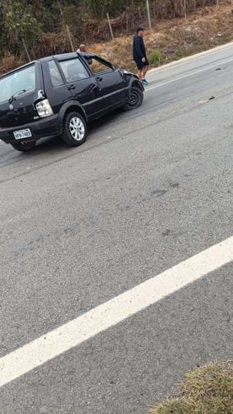 Um carro preto parado à beira da estrada, com uma pessoa em pé ao lado, no local de um capotamento.