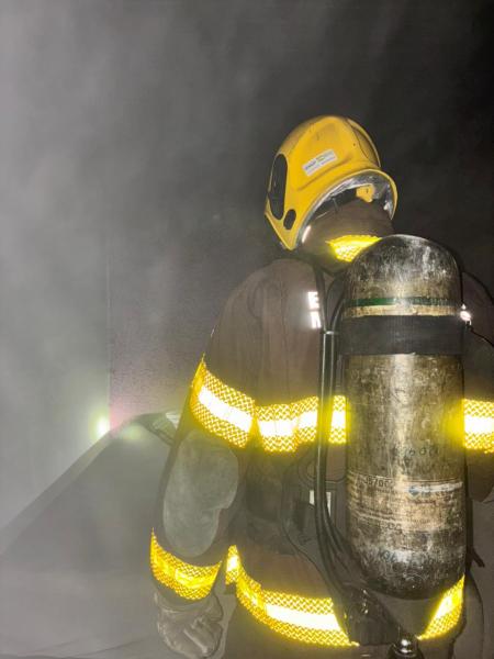 Bombeiro em traje de proteção e cilindro de ar, em ambiente com fumaça densa.