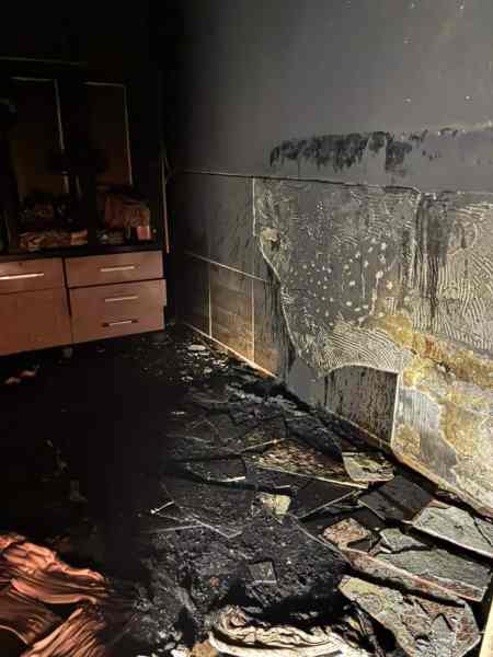 Ambiente de uma residência afetada por incêndio, com paredes e piso queimados, destroços visíveis e sujeira acumulada no chão.