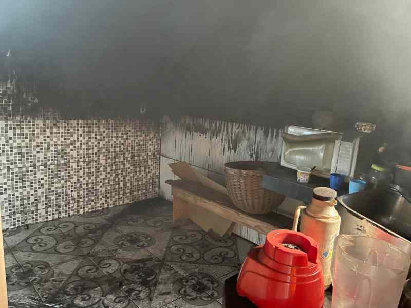 Cozinha afetada por incêndio, com paredes pretas e fumaça visível, mostrando danos e sujeira no ambiente.