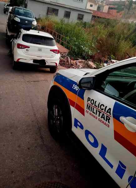 Imagem de um veículo da Polícia Militar de Minas Gerais em uma cena de abordagem. Dois carros, um Fiat Argo branco e um Fiat Uno preto, estão estacionados na via, com vegetação ao fundo.