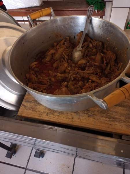 Panelada de carne cozida com molho, servida em uma panela grande de alumínio.