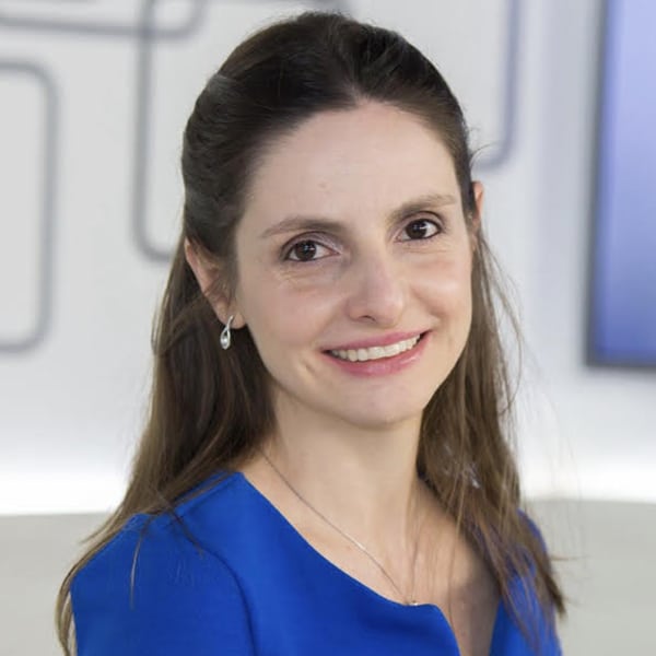 Retrato de uma mulher sorridente com cabelo longo e liso, usando uma blusa azul em um ambiente iluminado.