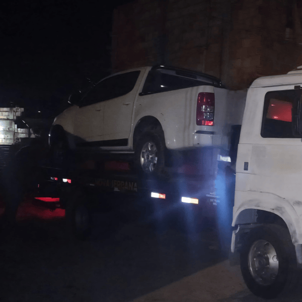 Caminhonete Chevrolet S10 branca sendo transportada em um reboque durante operação policial noturna.