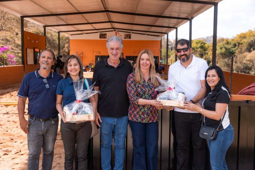Grupo de pessoas posando em um local com um fundo que parece ser uma instalação de equoterapia, segurando uma cesta de presente.