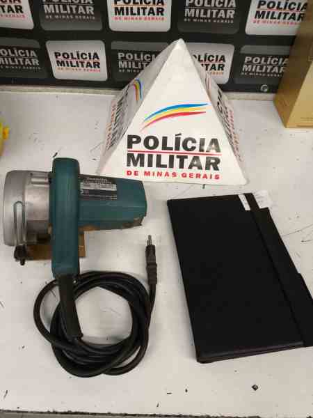 Equipamentos recuperados pela Polícia Militar, incluindo uma serra elétrica e um tablet, com uma placa da Polícia Militar de Minas Gerais ao fundo.