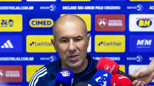 Treinador durante entrevista coletiva com microfones de diferentes emissoras ao fundo.
