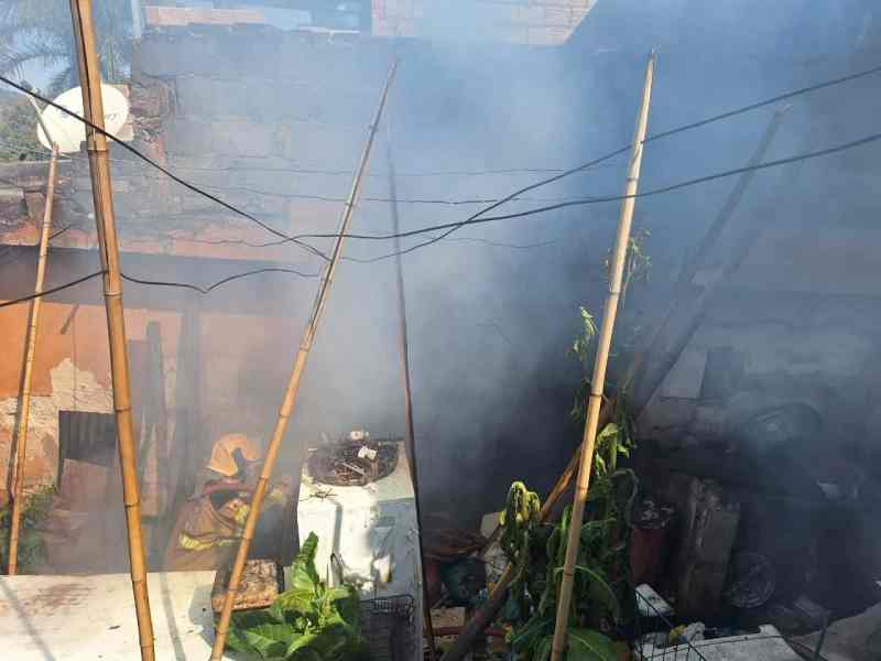 Cozinha de residência com fumaça densa, indicando um incêndio, cercada por bambus e materiais domésticos.
