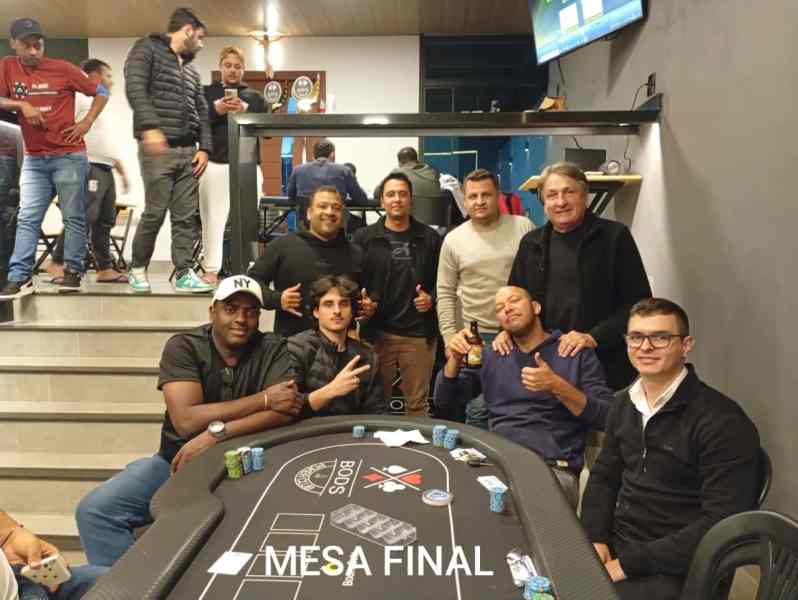 Mesa final do 8° Etapa do Torneio Regional de Poker PPBods em Divinópolis, com 9 jogadores sorrindo e posando para a foto ao redor de uma mesa de poker.