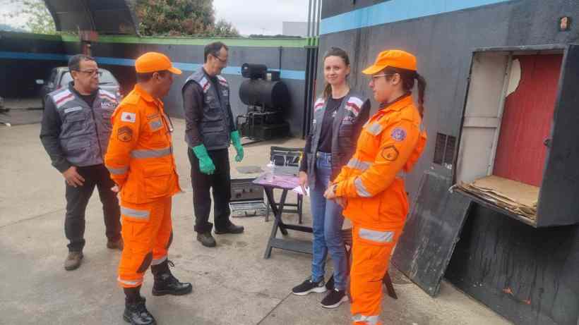 Grupo de profissionais, incluindo bombeiros e uma mulher, avaliando equipamentos em uma instalação, provavelmente durante uma operação de fiscalização de segurança contra incêndios.