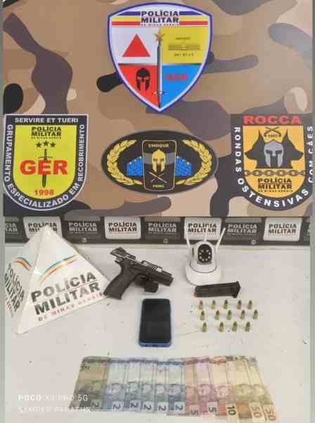 Imagem de uma mesa com uma pistola, um celular, uma câmera de segurança, dinheiro em notas e munições, com logos da Polícia Militar ao fundo.