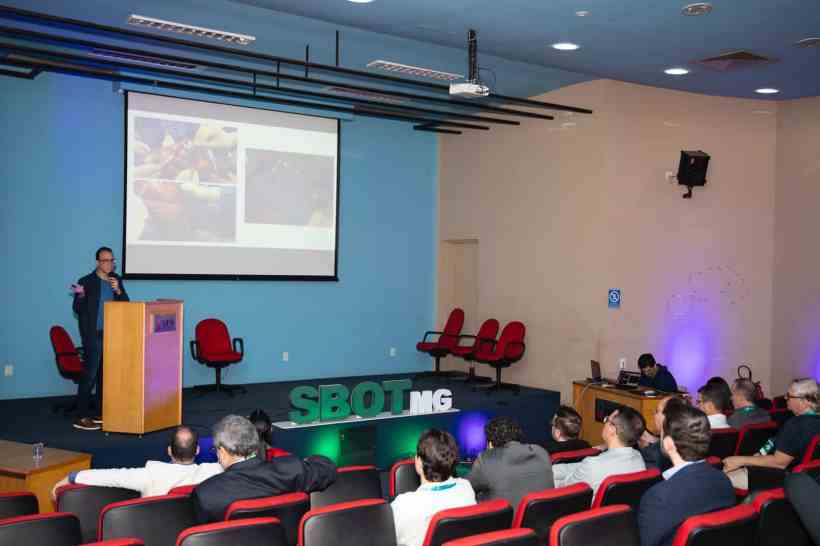 Palestrante apresentando a conferência com slides sobre técnicas cirúrgicas em ortopedia e traumatologia para uma audiência atenta em um auditório.