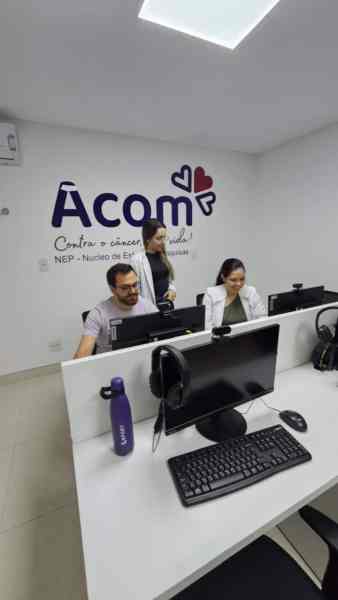 Equipe de trabalho no Núcleo de Estudos e Pesquisa da Acom, com pessoas em frente a computadores em ambiente clínico.