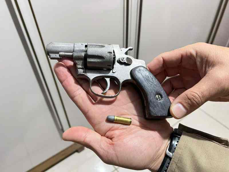 Uma mão segurando um revólver prateado calibre 32 com um cartucho ao lado.