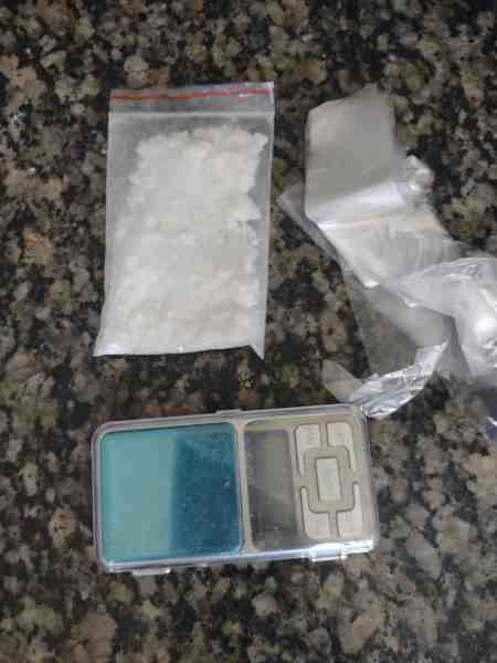 Imagem mostrando uma balança digital e porções de substância suspeita em embalagens transparentes, colocadas sobre uma superfície de granite.