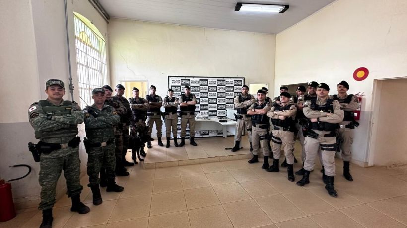 Um grupo de policiais em um ambiente interno, posando para a foto. Eles estão vestidos com uniformes de combate, alguns com armas e equipamentos táticos, demonstrando prontidão e segurança.