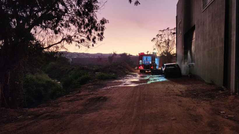 Caminhão do Corpo de Bombeiros combatendo incêndio em veículo em estrada de terra, ao amanhecer.