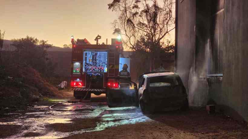 Um caminhão de bombeiros combatendo um incêndio em um veículo danificado em uma área escura e deserta.