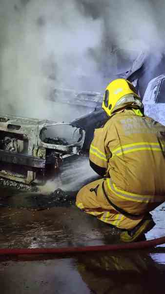 Um bombeiro em ação apagando um incêndio em um veículo, com fumaça saindo do carro danificado.
