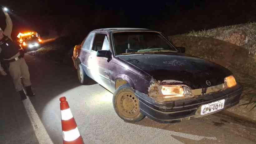 Veículo GM/Monza danificado parado na rodovia MG-050, com cones de sinalização e policial direcionando os tráfegos durante a noite.