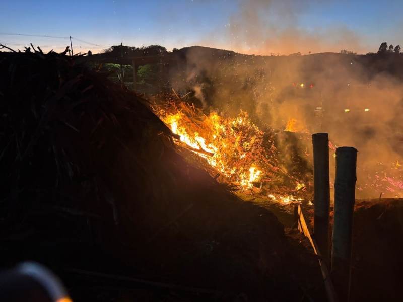 Incêndio em um amontoado de rejeitos de madeira, com chamas intensas e fumaça, em uma madeireira durante a madrugada.
