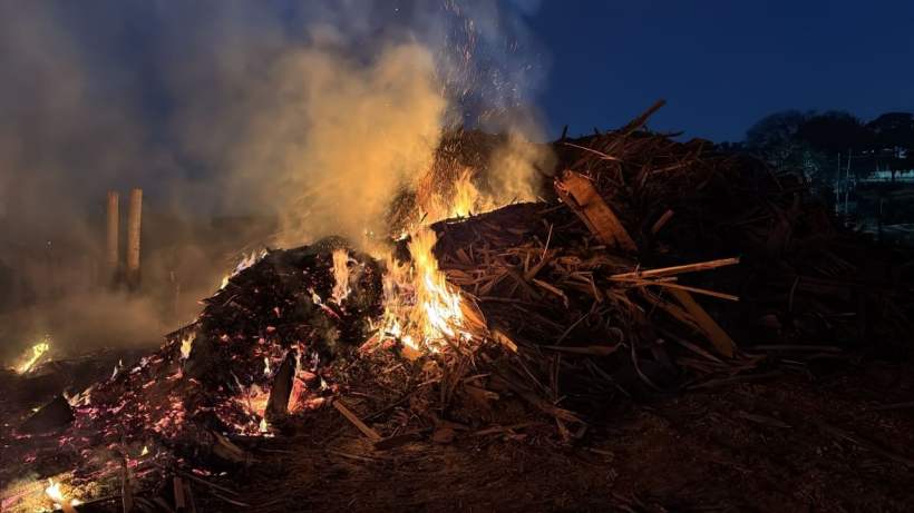 Incêndio em amontoado de rejeitos de madeira em uma madeireira, com fumaça e chamas visíveis, em Campo Belo, Minas Gerais.