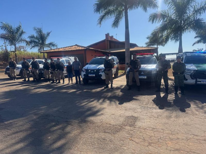 Militares da Polícia Militar de Minas Gerais em operação de segurança no campo, com veículos e equipes em frente a uma residência.