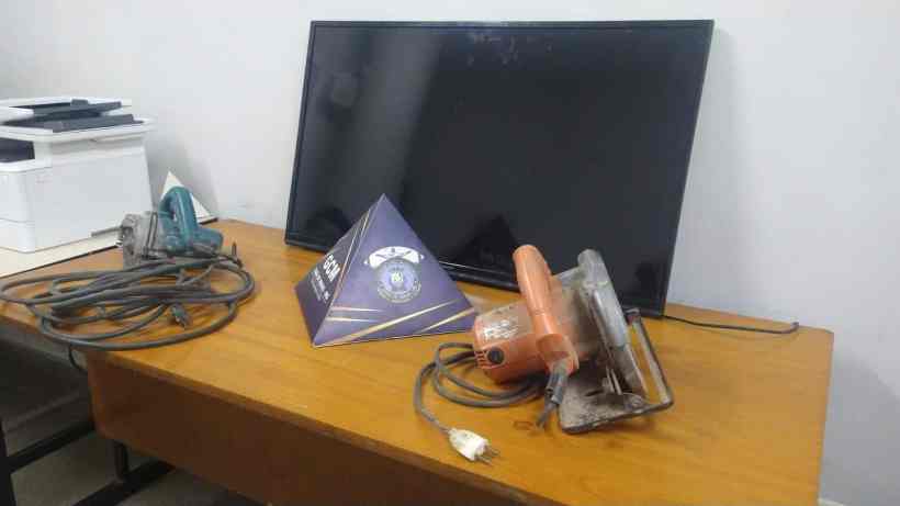 Objetos recuperados pela Guarda Civil Municipal de Pará de Minas, incluindo uma televisão, uma serra circular e uma maquita, sobre uma mesa em um ambiente policial.