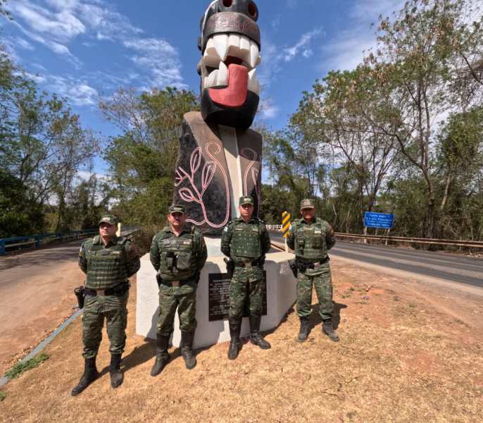 Quatro policiais militares da Polícia Militar de Meio Ambiente de Minas Gerais posam em frente a um monumento estilizado, rodeados por vegetação, sob um céu claro.