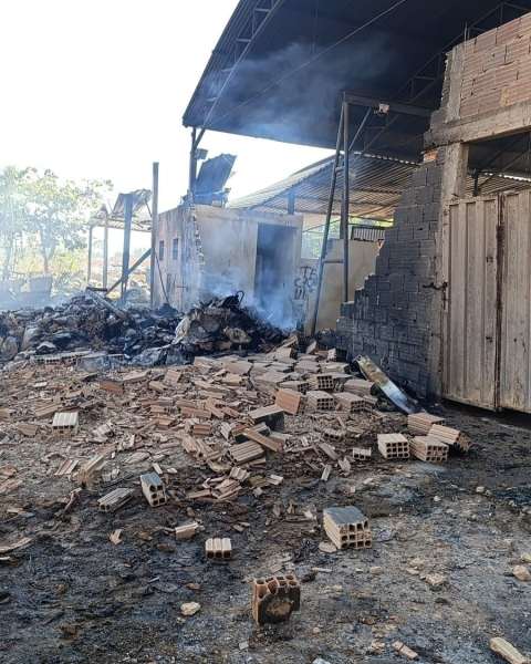 Área de disposição de resíduos sólidos com danos causados por incêndio, incluindo escombros e fumaça visível.