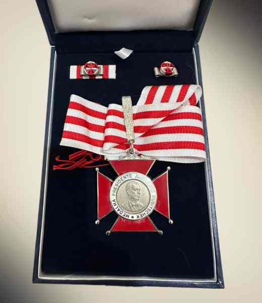 Medalha Presidente Juscelino Kubitschek em uma caixa de apresentação, com fita de faixa vermelha e branca, acompanhada por insígnias.