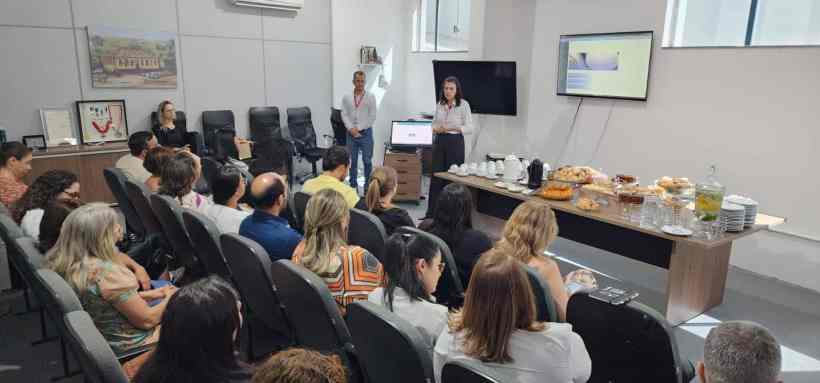 Reunião do 1° Café com Secretários, com participantes sentados e apresentadores em pé, discutindo inovações na gestão regional de saúde, com mesa de café da manhã ao fundo.