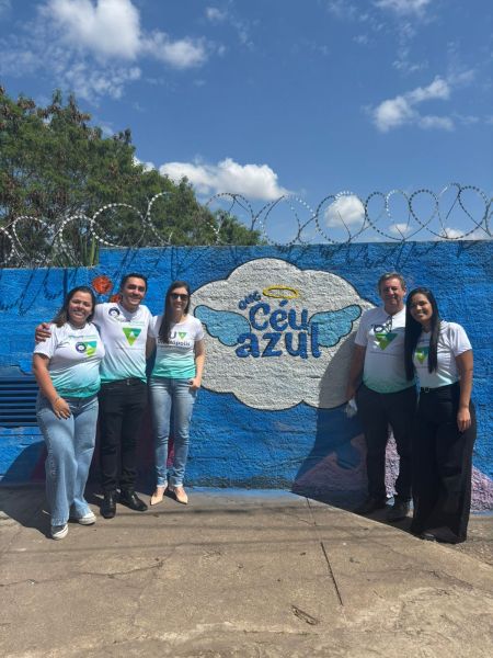Grupo de voluntários posando em frente ao mural colorido 'Céu Azul', após revitalização da instituição.