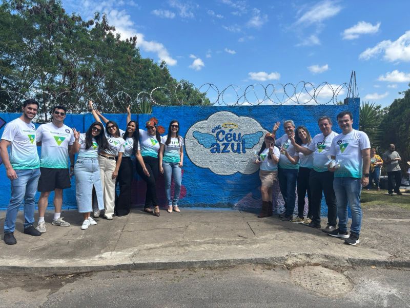Grupo de voluntários posando em frente a um mural colorido com a inscrição 'Céu Azul' e desenhos de asas, durante a revitalização de uma instituição para crianças com autismo.