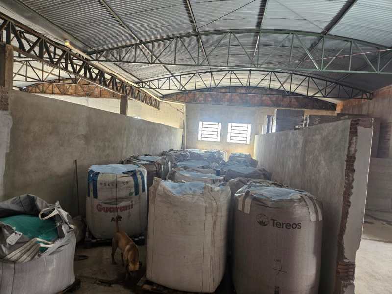 Interior de uma fábrica clandestina com sacos grandes de sabão em pó falsificado, mostrando uma estrutura simples e vazia.