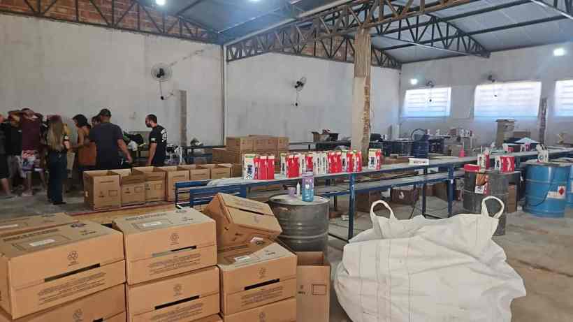 Interior de uma fábrica clandestina de sabão em pó falsificado, com caixas empilhadas e produtos dispostos em mesas, durante uma operação policial.