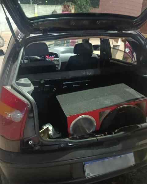 Imagem do porta-malas de um Fiat Palio, mostrando equipamentos de som automotivo, incluindo um sistema de caixas acústicas.