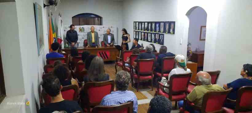 Evento com mesa redonda e palestrantes, com público sentado em cadeiras em uma sala decorada, promovendo o Fliarte – Festival de Literatura e Artes.