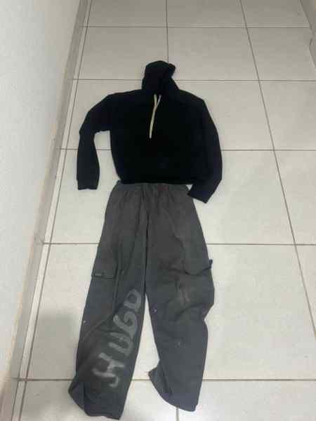 Roupa apreendida, incluindo um moletom preto e calças cinzas, dispostas sobre um piso de azulejos brancos.