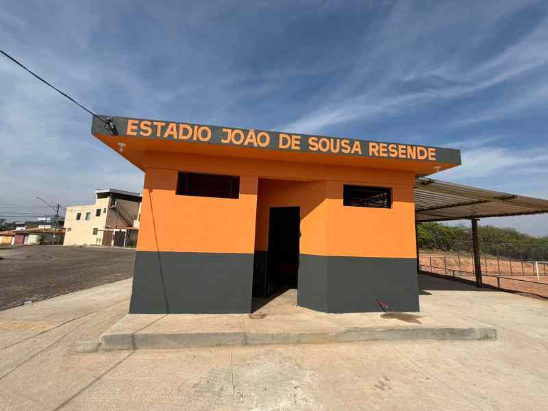 Fachada do Estádio João de Sousa Resende, pintada em laranja e cinza, com céu azul ao fundo.
