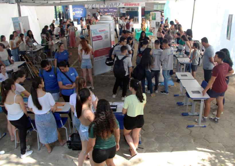 Vista da Feira de Profissões da UEMG em Divinópolis, com várias pessoas interagindo em estandes e mesas, promovendo cursos e atividades acadêmicas.