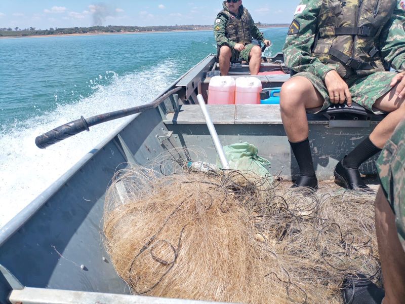 Policiais em uma embarcação durante a operação contra a pesca predatória, com redes de pesca apreendidas à vista.