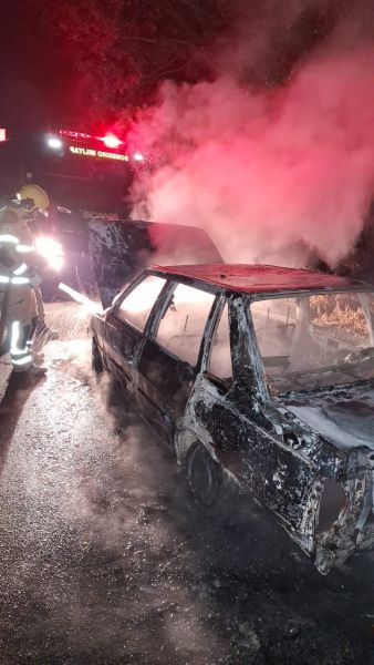 Veículo em chamas na rodovia BR-332, com bombeiros trabalhando no combate ao incêndio, destacando fumaça e danos significativos ao carro.