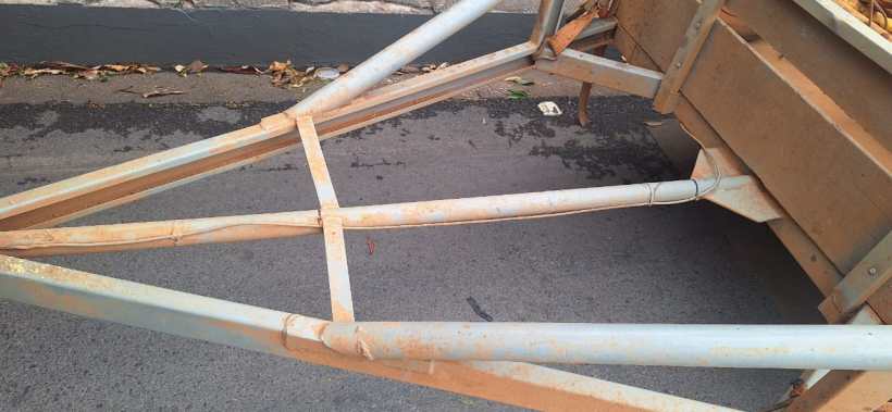 Visão de uma estrutura metálica de reboque de caminhão, com detalhes de corrosão e desgaste, sobre uma superfície de asfalto.