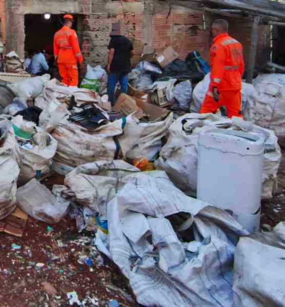Agentes da Polícia Militar e Corpo de Bombeiros em operação de fiscalização em local com material descartado, incluindo sacos de lixo e itens metálicos.