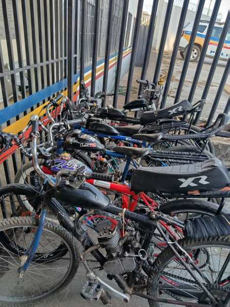 Várias bicicletas estacionadas atrás de uma grade, com destaque para as bicicletas equipadas com motores visíveis.