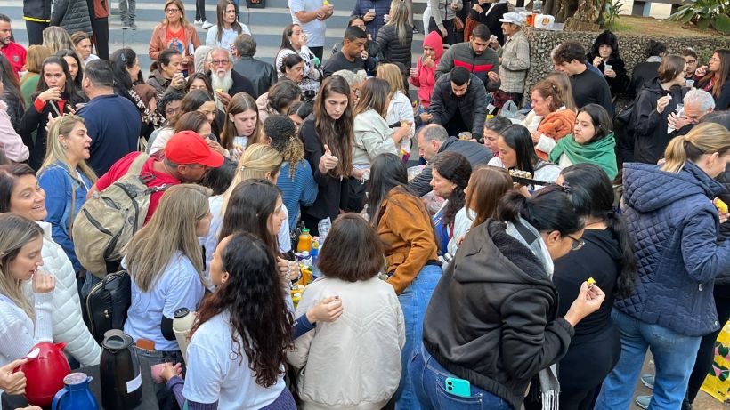 A large crowd of people gathered outdoors, participating in a lively social event. Attendees are seen engaging with each other, holding drinks and food, showcasing a festive atmosphere.